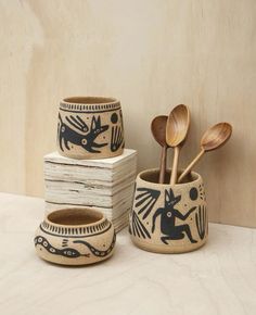 three wooden spoons and two cups with designs on them, one is holding utensils