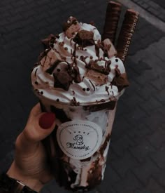 a person holding up a chocolate milkshake with whipped cream and cookies on top