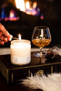 a person lighting a candle next to a glass of wine