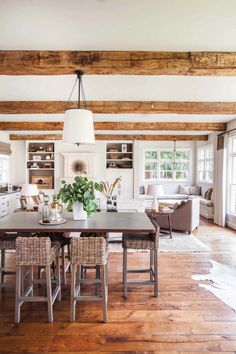 an open concept living room and dining area with wood flooring, white walls, large windows, and wooden beams