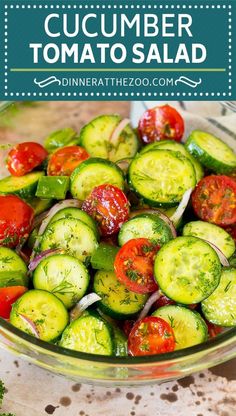 a glass bowl filled with cucumbers and tomatoes on top of a table next to broccoli