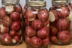 three jars filled with red potatoes sitting on top of a wooden table