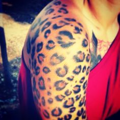 a woman wearing a red shirt has a leopard print tattoo on her arm and shoulder