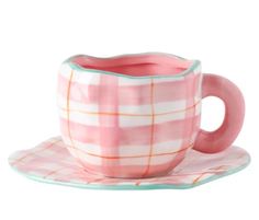 a pink cup and saucer sitting on top of a white plate with a checkered design