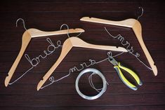 two wooden clothes hangers, scissors and wire on a wood floor with the words bride and groom written in cursive writing