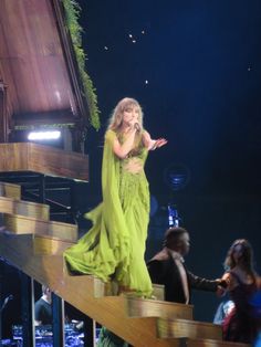 a woman in a green dress standing on stairs with her hands out to the crowd