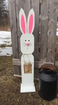 a wooden bunny standing next to a potted plant in front of a wood fence