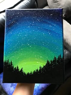 someone is holding up a painting with the stars in the night sky and trees on it