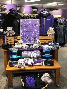 a purple and white sign sitting on top of a wooden table in a store filled with clothing