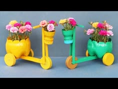 three colorful flower pots sitting on wheels with flowers in the middle one is yellow and the other two are green