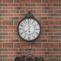 a large clock mounted to the side of a brick wall next to a small table