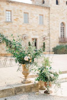 two vases filled with flowers sitting on the steps in front of a stone building