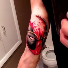 a man's arm with a deadpool tattoo on it and a toilet in the background