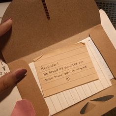 a person holding a piece of paper with writing on it in a cardboard box next to a pair of scissors