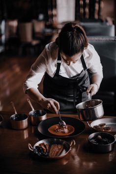 a woman in an apron preparing food on top of a wooden table next to pots and pans