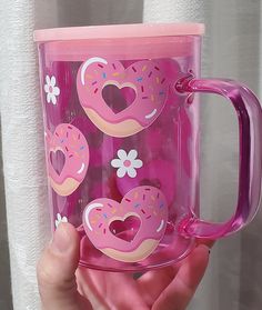 a hand holding a pink coffee mug with donuts on it and hearts painted on the inside