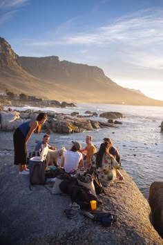 a group of people sitting on top of a rock next to the ocean