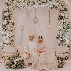 a man and woman sitting next to each other in front of a flower covered stage