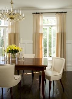 a dining room table with chairs and a chandelier in front of two windows