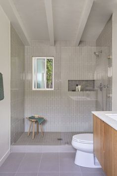 a white toilet sitting next to a bathroom sink under a window in a room with tile floors