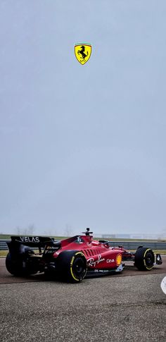 a red race car is on the track with a yellow and black kite in the sky