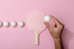 a person holding a ping pong paddle in front of five white balls on a pink background