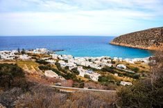 an aerial view of a small town by the ocean with blue water and hills in the background