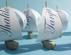 three wooden sailboats with blue lettering on them sitting side by side in front of a blue background