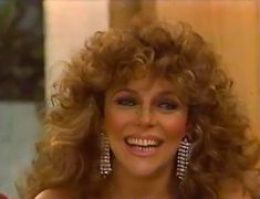 an old photo of a woman with curly hair and big earrings smiling at the camera