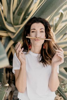 a woman standing in front of a cactus holding a stick to her mouth and looking at the camera