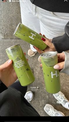 two people holding up green drinks with the words h in white on them and an image of