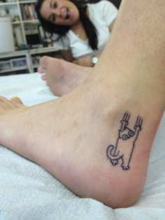 a woman laying in bed with a tattoo on her foot that has a cat drawn on it