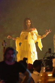 a woman in a yellow dress standing on stage with her hands out to the crowd