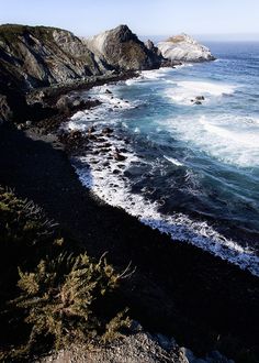 an ocean view from the top of a hill with waves crashing on it and rocks in the foreground