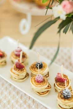 small pancakes with strawberries and blueberries are on a white plate next to flowers