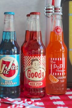 three bottles of soda sitting on top of a red and white checkered table cloth