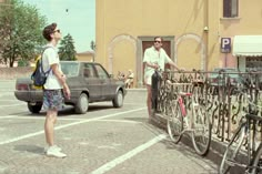 two people standing in front of a parking lot with bicycles on the rack and cars parked behind them