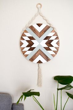 a wall hanging made out of wood and rope with a geometric design on it, next to a potted plant