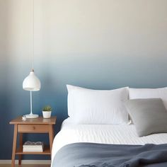 a bed with white sheets and pillows in a bedroom next to a blue painted wall