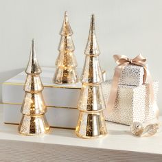 three gold christmas trees sitting on top of a white shelf next to a present box