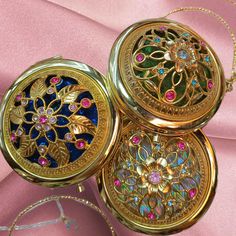 three gold lockes with different designs on them sitting on a pink cloth covered surface