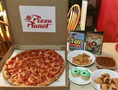 a pizza in a box with other food items around it and a toy story book on the table