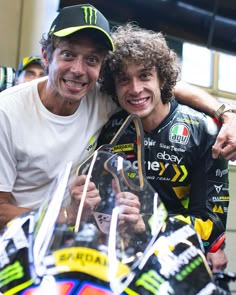 two men are hugging each other while posing for a photo with a motorcycle helmet on