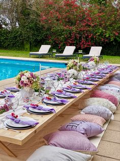 a long table is set with plates and place settings for an outdoor dinner by the pool