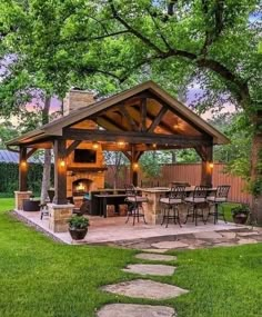 an outdoor kitchen and grill area in the middle of a yard with grass, rocks and trees