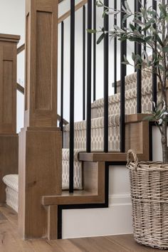 a wooden stair case next to a basket with a plant in it on the floor