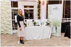 a woman standing next to a table with pictures on it and flowers in the background