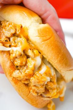 a hand holding a sandwich with chicken, cheese and onions in it on a white plate