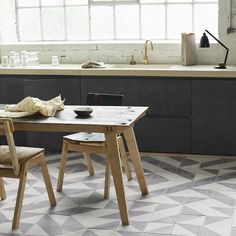 a kitchen with black and white tile flooring next to a wooden table in front of a window