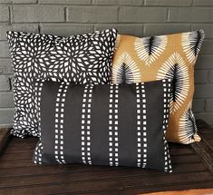 three black and white pillows sitting on top of a wooden table next to a brick wall